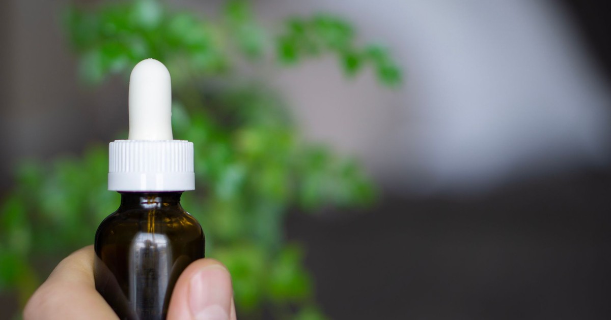 Hand holding a dropper bottle of CBD oil against a soft-focus botanical background.