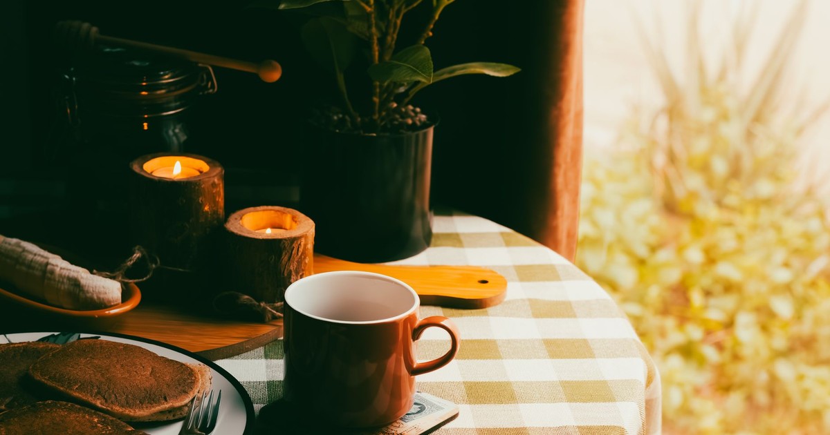 Warm and inviting breakfast setting with coffee, pancakes, and candles on a checkered tablecloth.