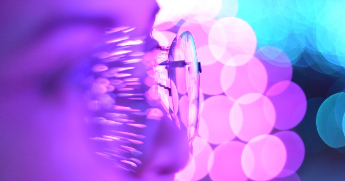 Close-up photo of eyeglasses with bright purple and blue bokeh lights creating an abstract aesthetic.