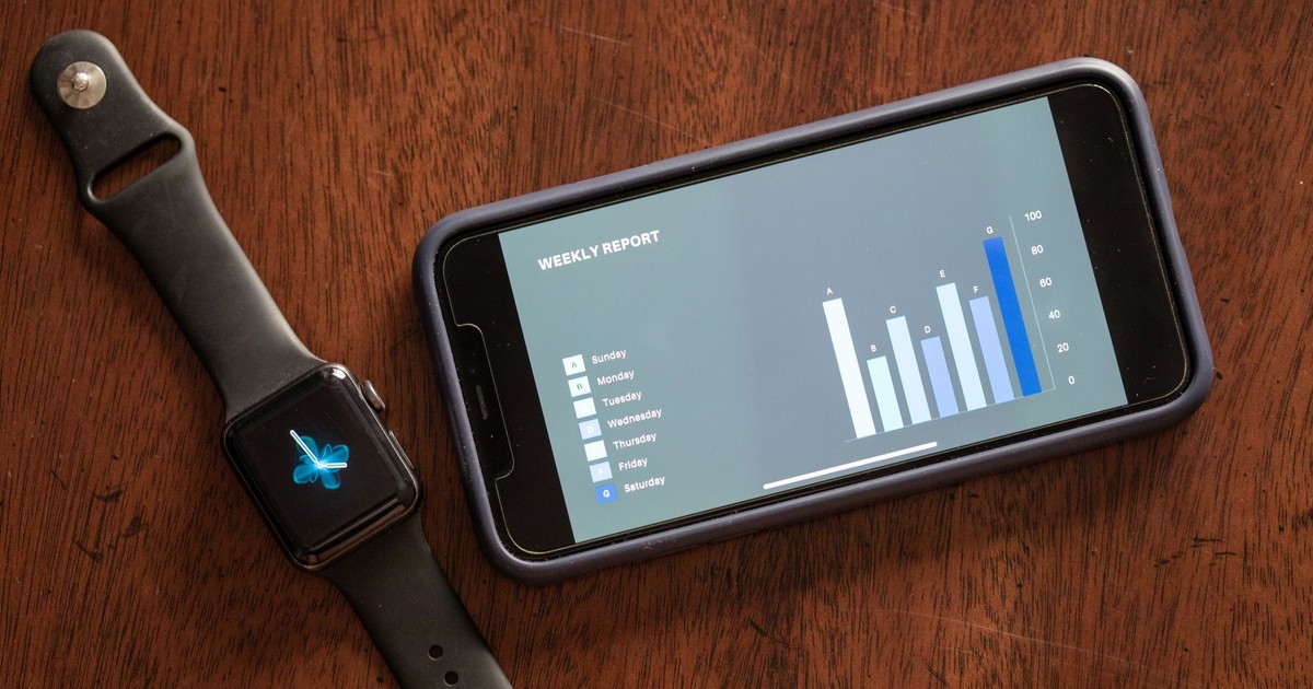 Close-up of a smartphone and smartwatch displaying a weekly report on a wooden table.