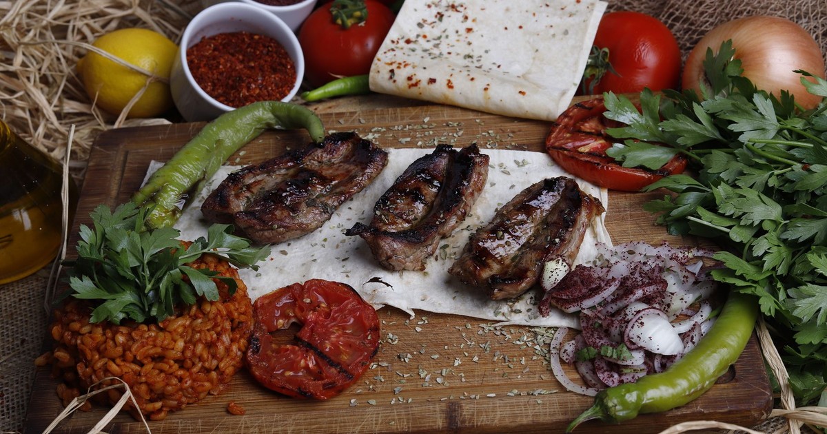 Delicious grilled meat served with fresh vegetables, herbs, and spices on a rustic cutting board.