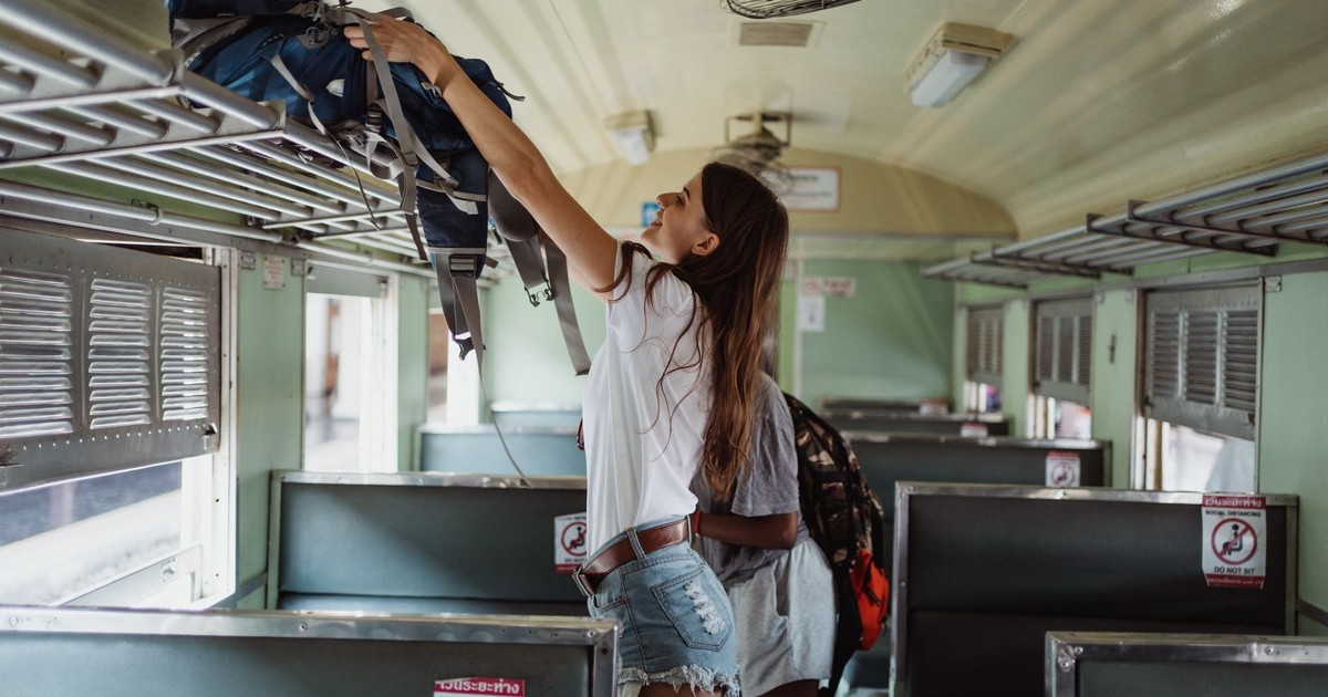 Woman placing backpack on luggage rack inside an empty train carriage.
