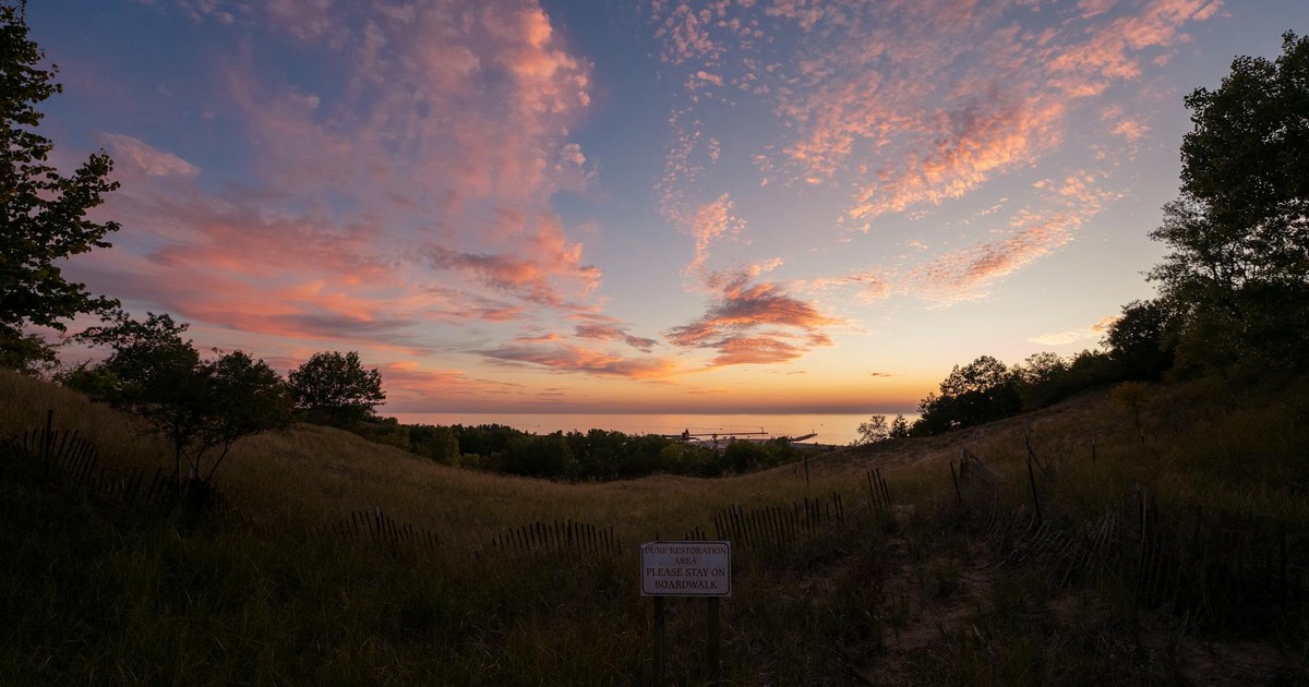 Dramatic sunset over Mount Pisgah dunes in Holland, Michigan with vibrant clouds and serene landscape.
