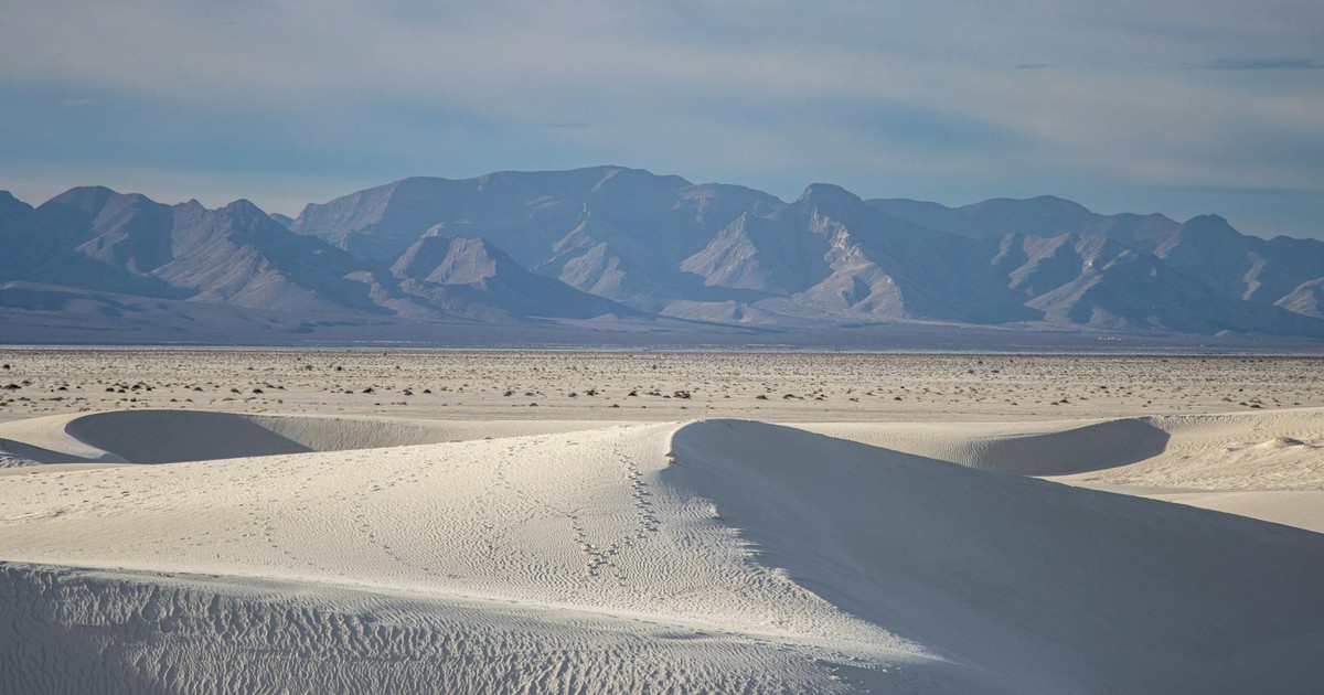 Expansive view of white sand dunes against distant mountains under a serene blue sky.