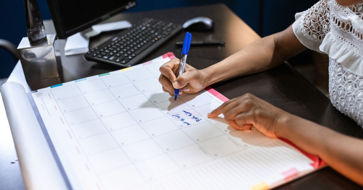 Person writing important notes in a desk calendar with a pen, set in an office.