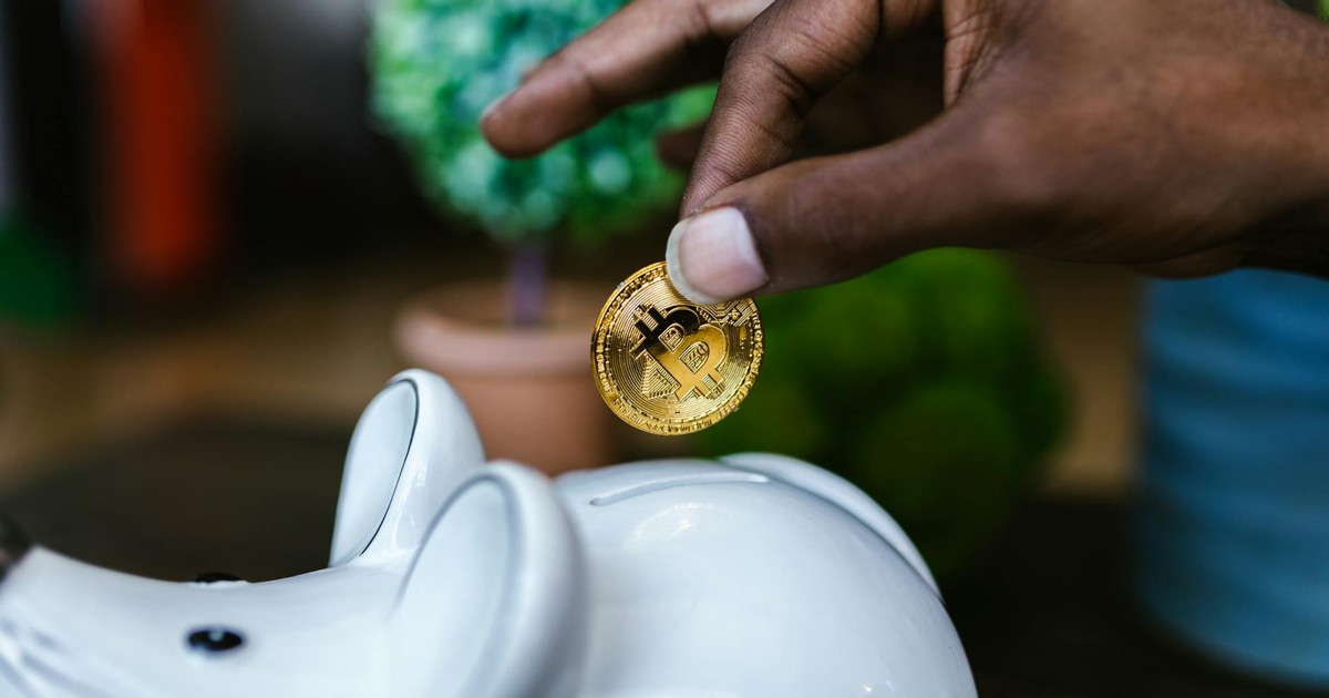 A close-up of a hand placing a bitcoin into a white piggy bank, symbolizing investment and savings.