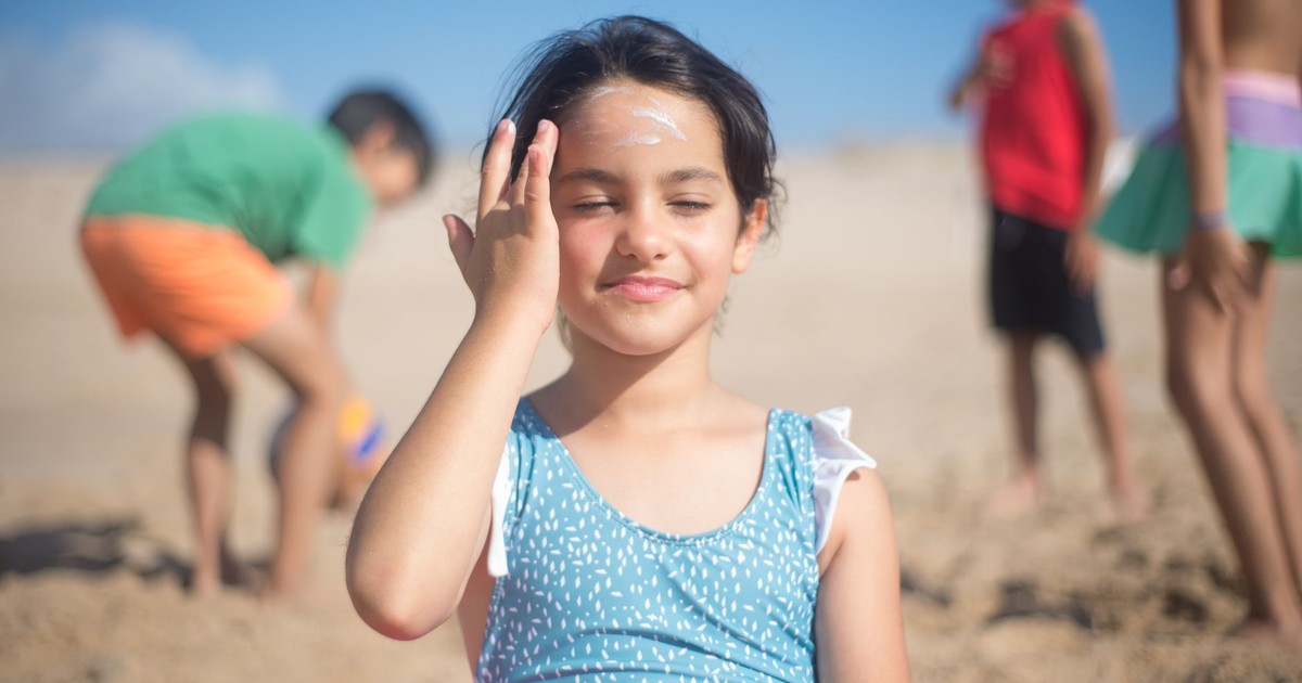 Young girl applying sunscreen at a beach in Portugal with friends playing in the sand.