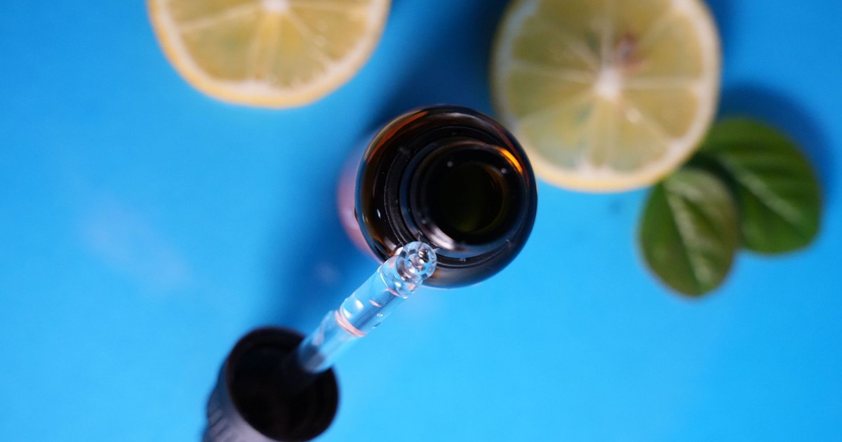 Close-up of dropper bottle with lemon slices on blue backdrop. Ideal for skincare or wellness themes.