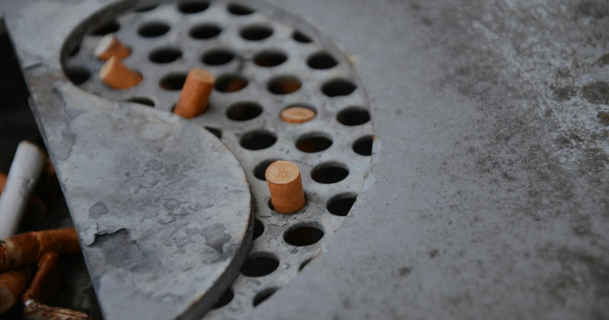 Detailed view of cigarette butts in a metal ashtray with perforated design, depicting usage and waste.