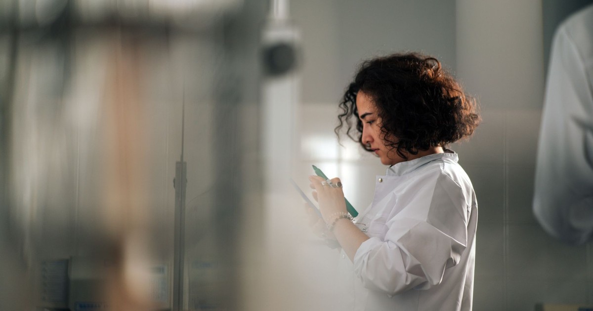 A focused female scientist with curly hair writes notes in a laboratory setting.