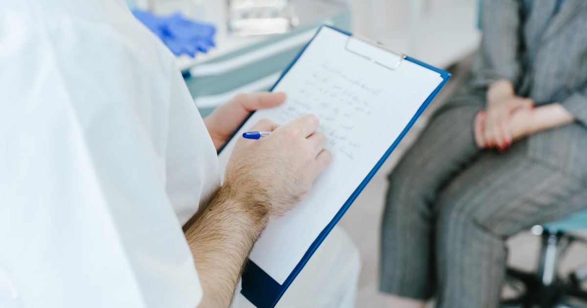 Medical professional writing patient notes on clipboard during consultation.