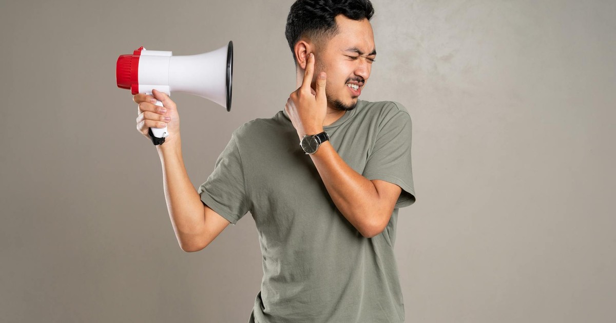 A man with a megaphone holding ear in discomfort, representing noise pollution or loud sounds.