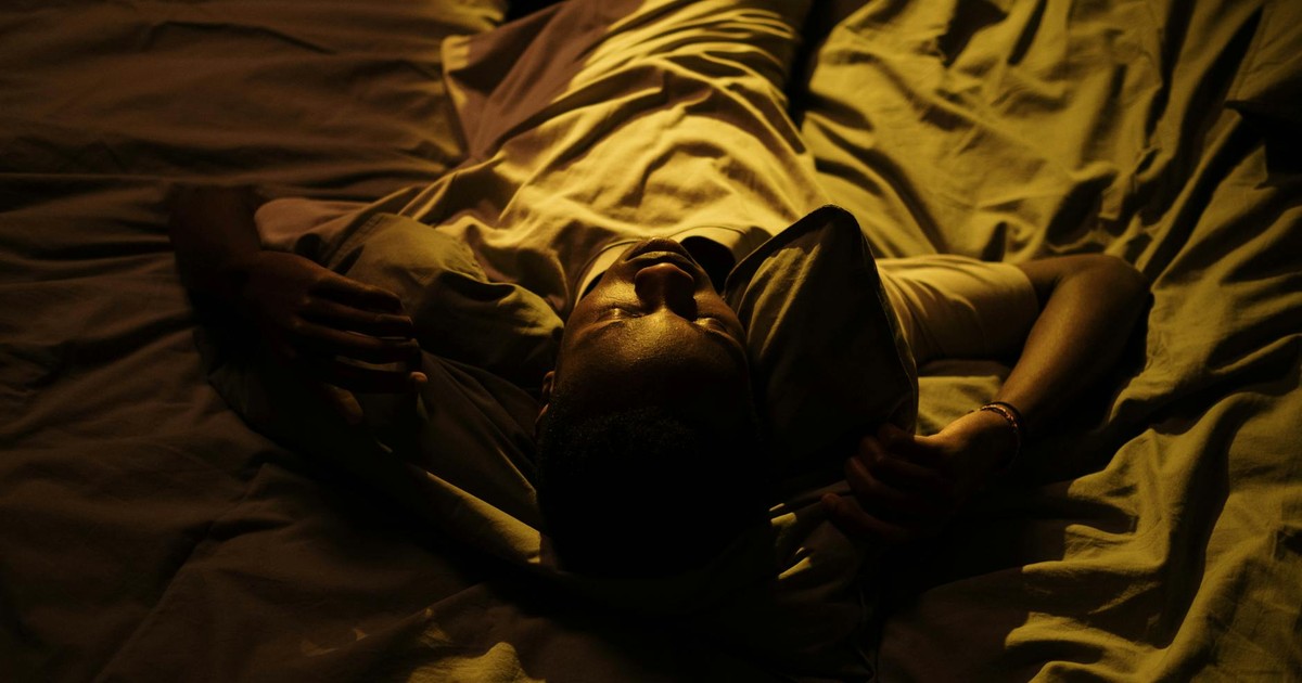 A man lies in bed at night, struggling with insomnia in a dimly lit room.