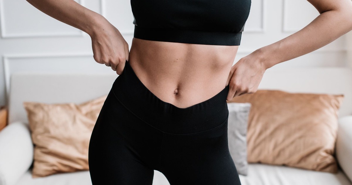 Close-up of a woman in activewear adjusting her pants in a stylish living room.
