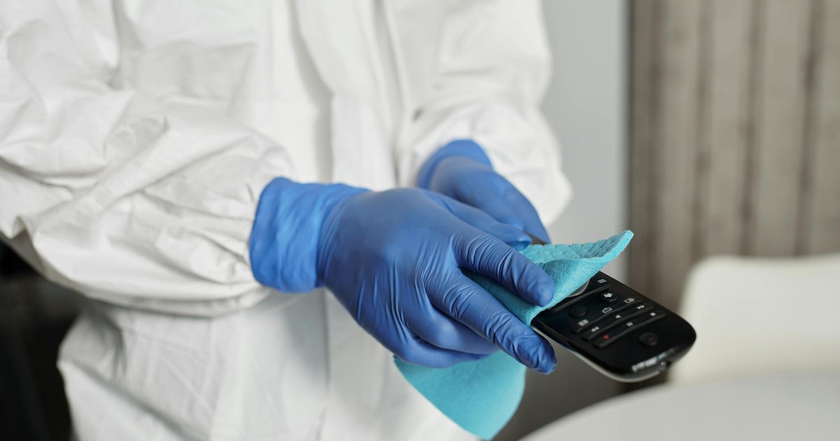 Close-up of a person disinfecting a remote control wearing protective gloves, ensuring cleanliness.
