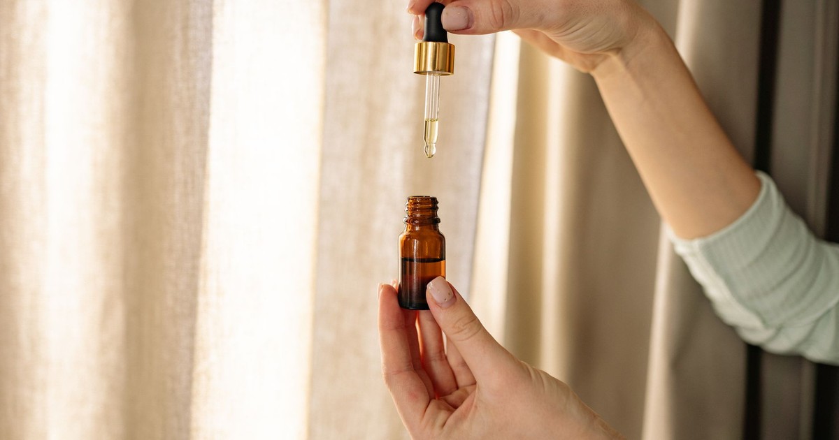 Close-up of hands holding a dropper and amber bottle for skincare product.