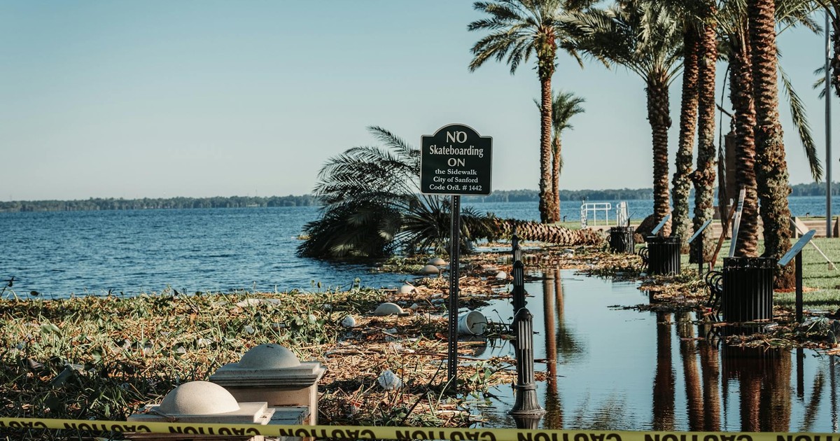 A flooded pathway with caution tape and palm trees by a lake in Sanford, Florida.