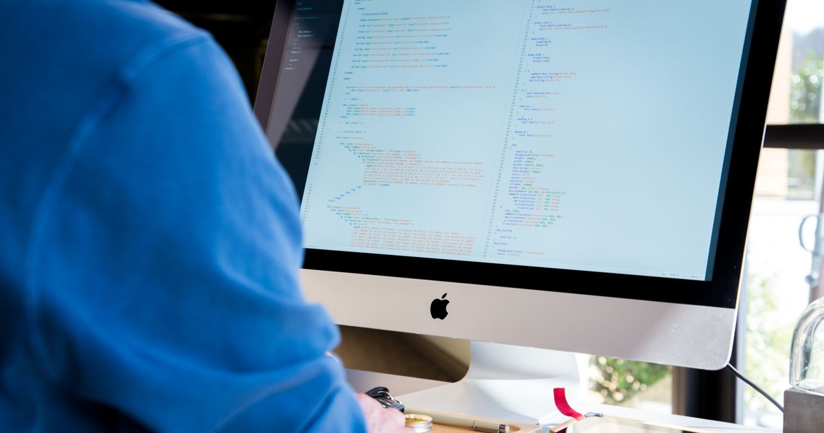 A programmer in a blue shirt coding on an iMac. Perfect for technology or work-related themes.