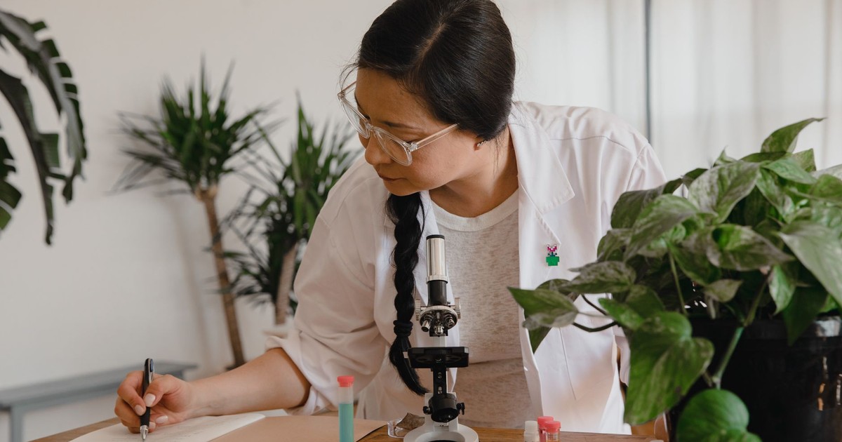 Female scientist conducting research and taking notes with microscope and plants.