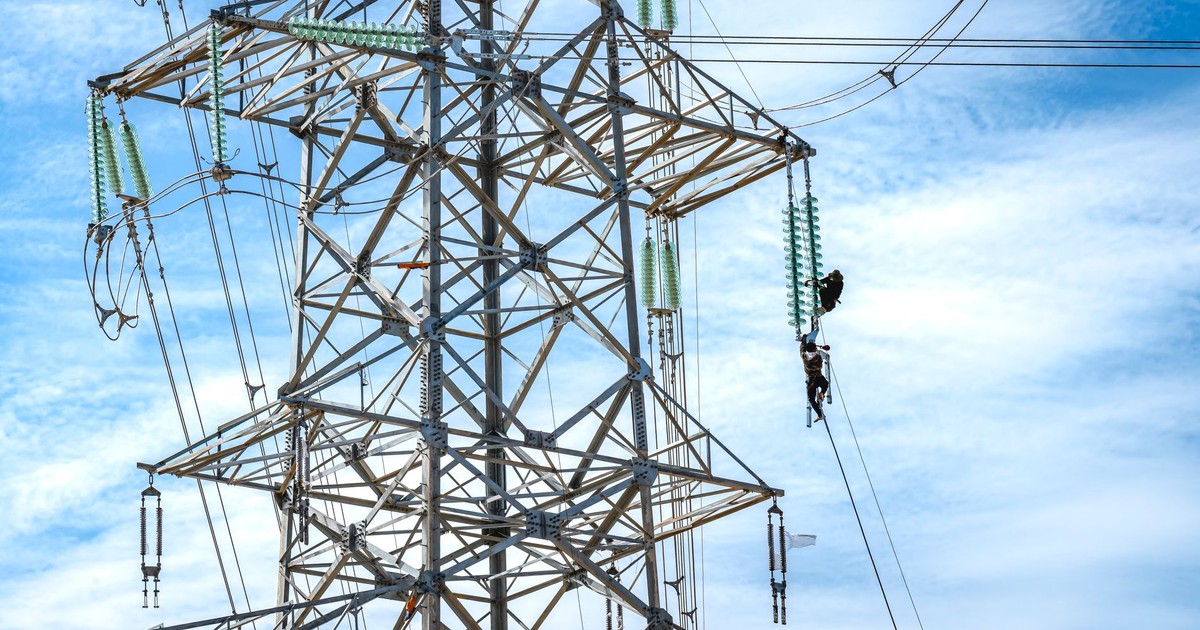 Workers performing maintenance on a high voltage power line against a blue sky.