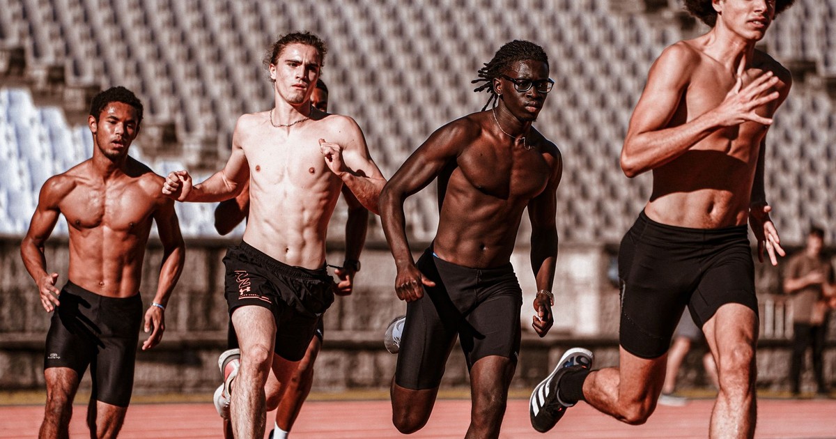 Four athletic men running on a sunny day at an outdoor track race, showcasing diversity.