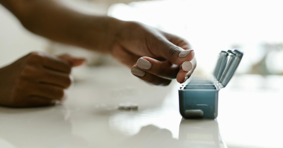 Hand placing pills in a weekly organizer, emphasizing medication management.