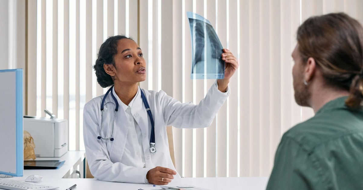 Female doctor examines x-ray results with male patient in a medical setting.