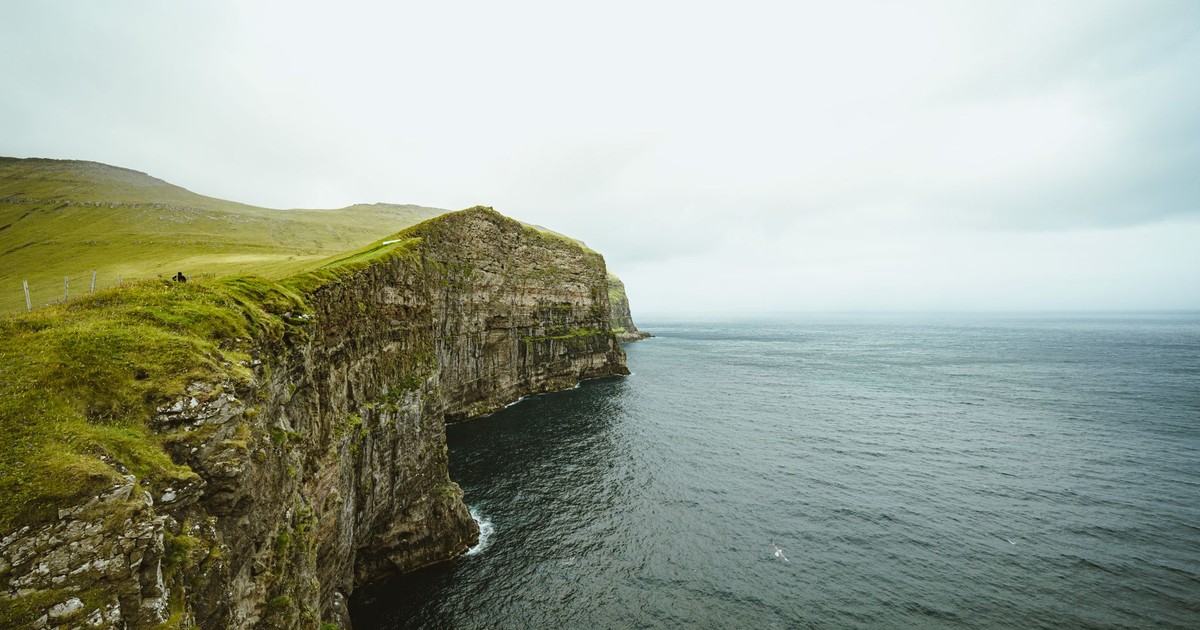 Majestic cliffs with lush greenery, overlooking a serene sea on an overcast day, perfect for nature enthusiasts.