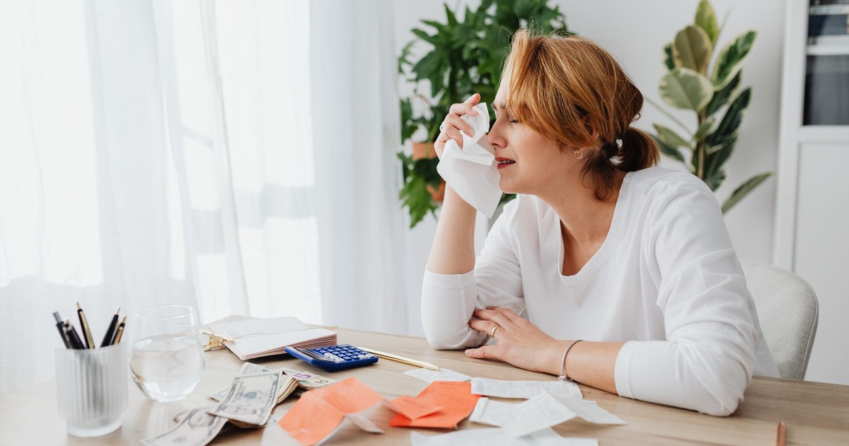 A woman is overwhelmed by bills and finances, sitting at a desk indoors.