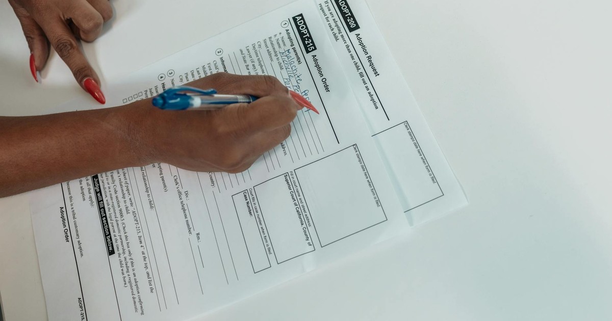 Close-up of a hand filling out an adoption request form with a pen.