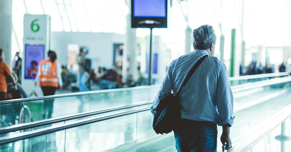 An adult male walking on an airport travelator, captured in a modern and well-lit terminal.