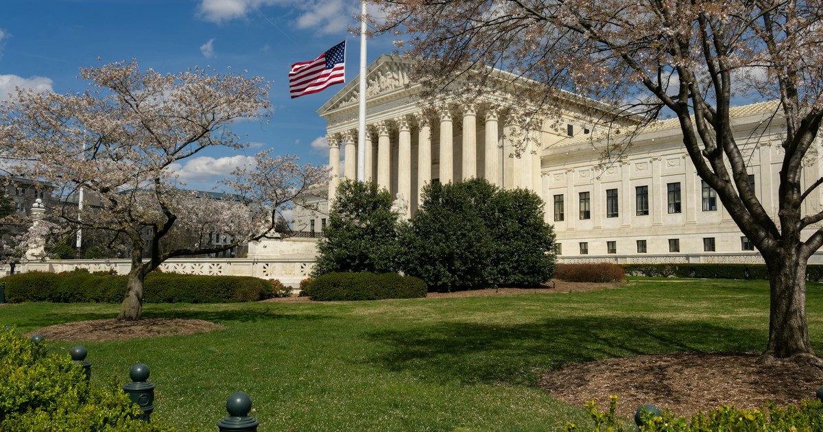 A view of a neoclassical government building with an American flag and cherry blossoms in Washington, DC.