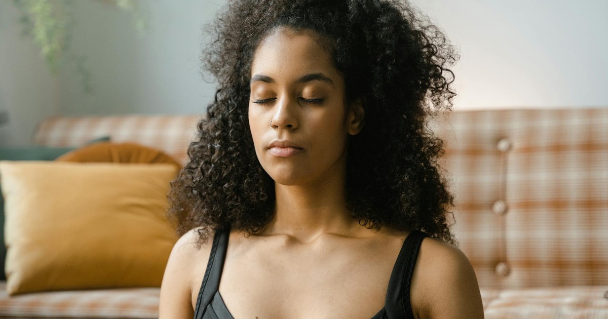 A woman with curly hair meditating indoors with eyes closed. Calm and serene setting.