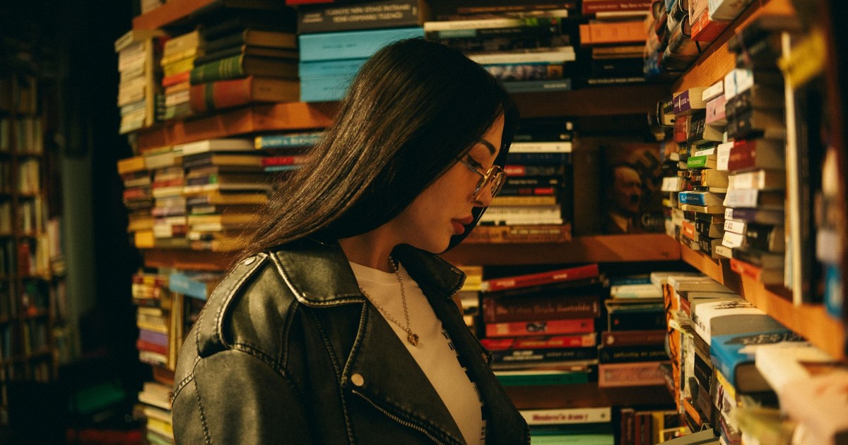 A woman engrossed in reading amidst a cozy bookstore with stacked shelves.