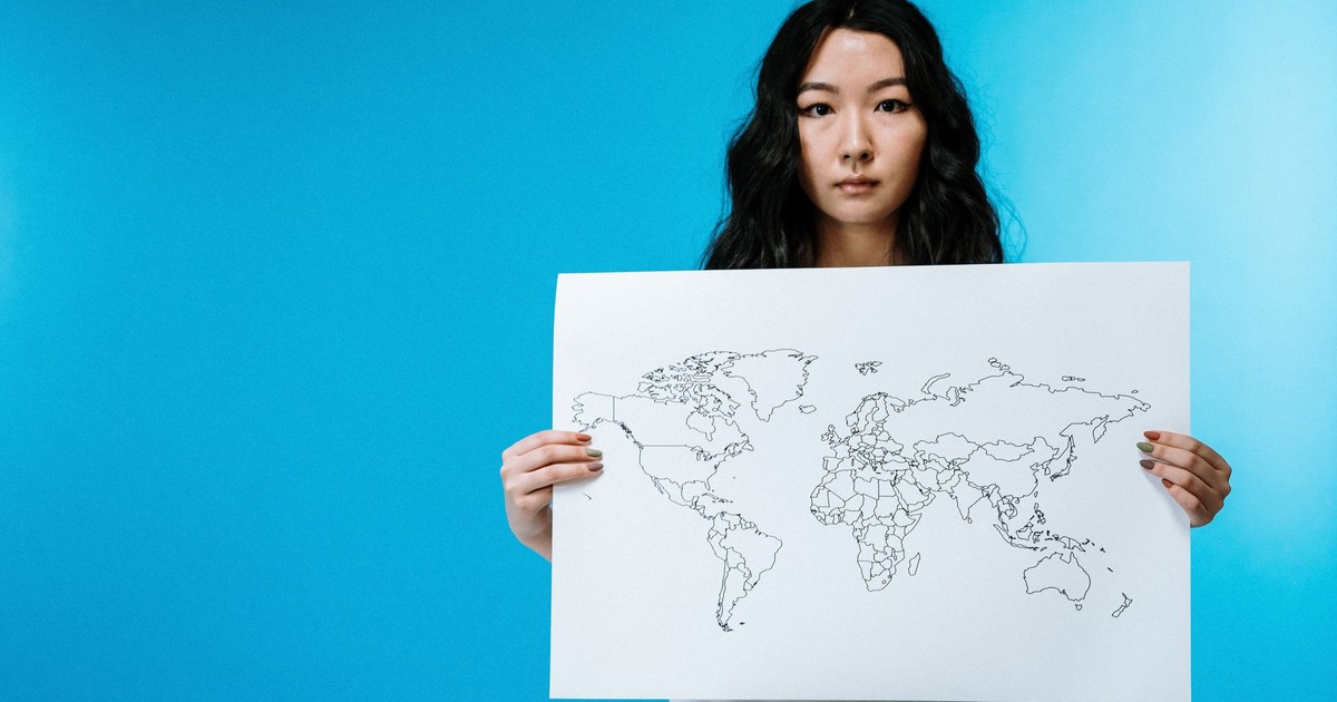 Portrait of a young woman holding a world map against a vivid blue background.