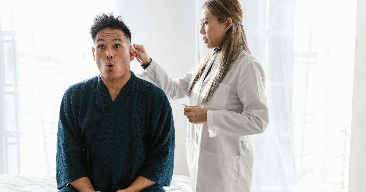 A doctor in a white coat conducts an ear exam on a patient indoors.