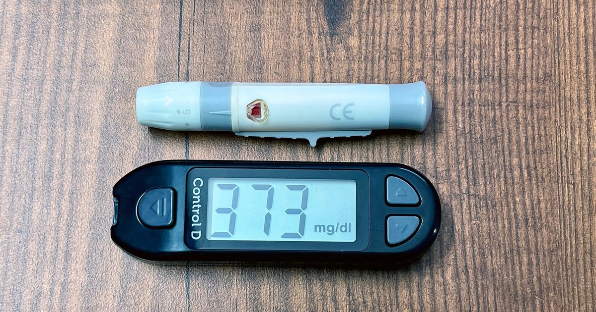 A digital glucometer and lancing device on a wooden surface indicating high blood glucose level.