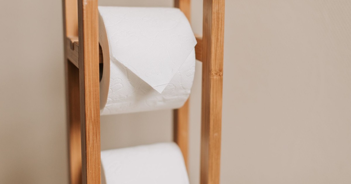 Wooden rack holding two toilet paper rolls in a minimalistic bathroom setting.