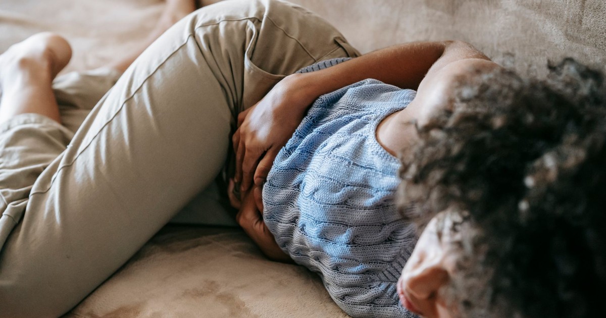From above of crop anonymous African American female lying on couch and touching belly while having stomach ache