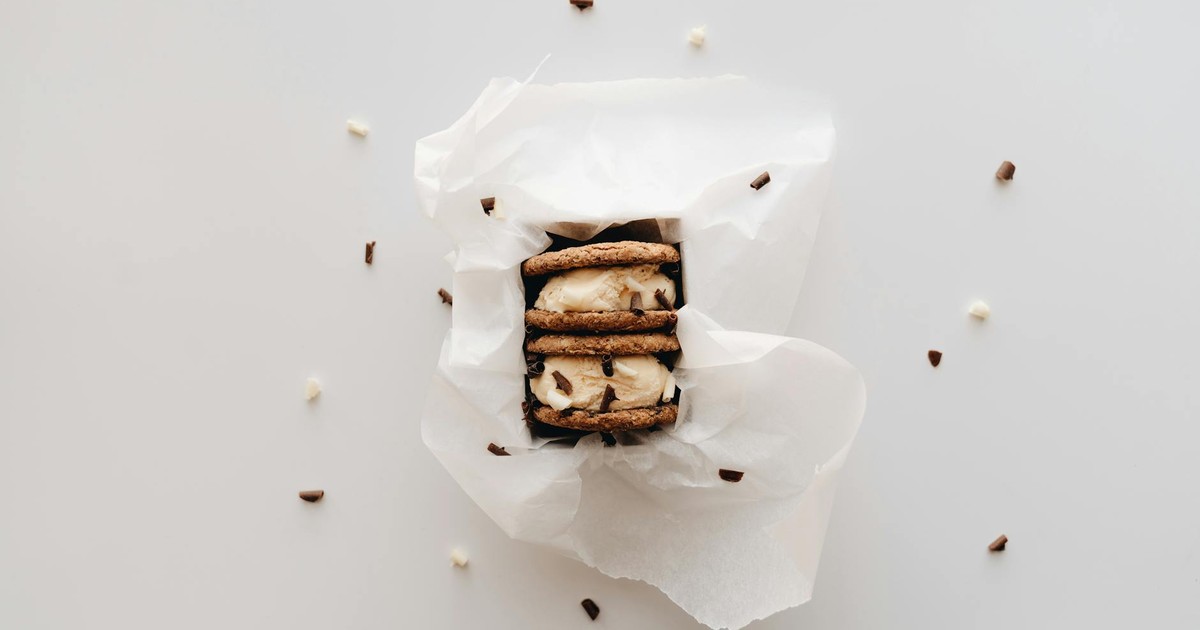 Close-up of a cookie sandwich ice cream wrapped in white paper, surrounded by chocolate sprinkles.