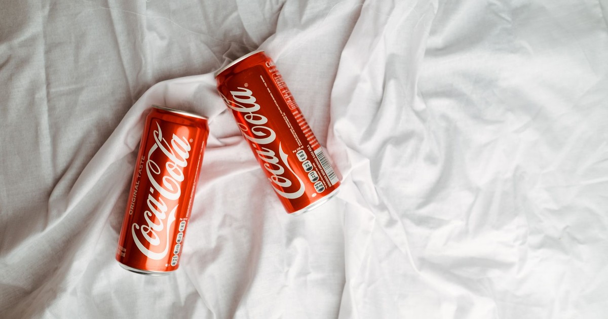 Two Coca Cola cans placed on a crumpled white textile, showcasing a classic beverage design.