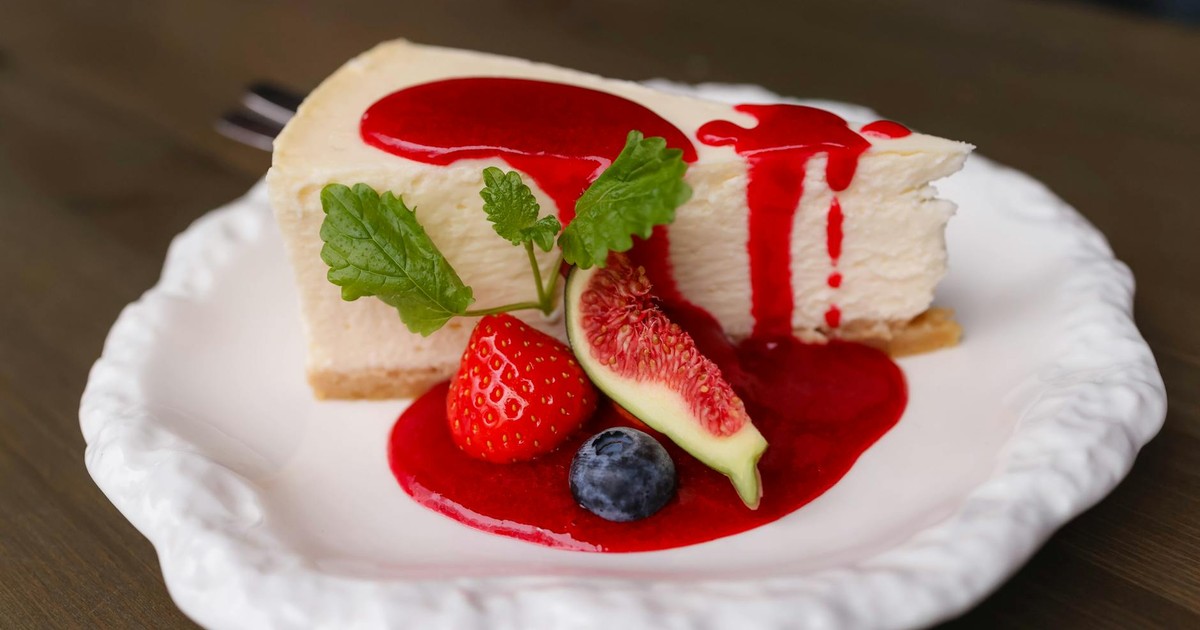 Creamy cheesecake with berries and fig on a white plate. Topped with red fruit sauce.