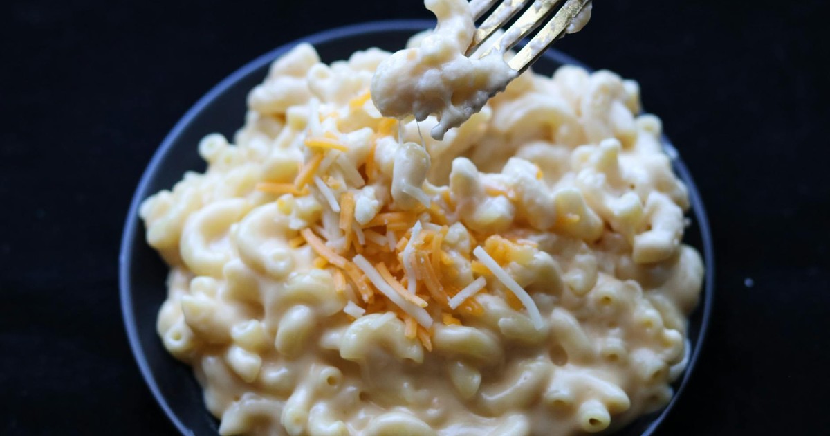 Delicious creamy mac and cheese topped with shredded cheese on a black plate.
