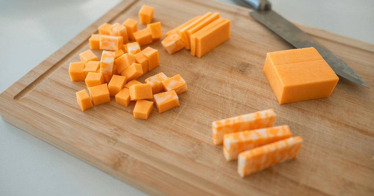 Close-up of cheddar and colby-jack cheese slices on a wooden cutting board with a knife.