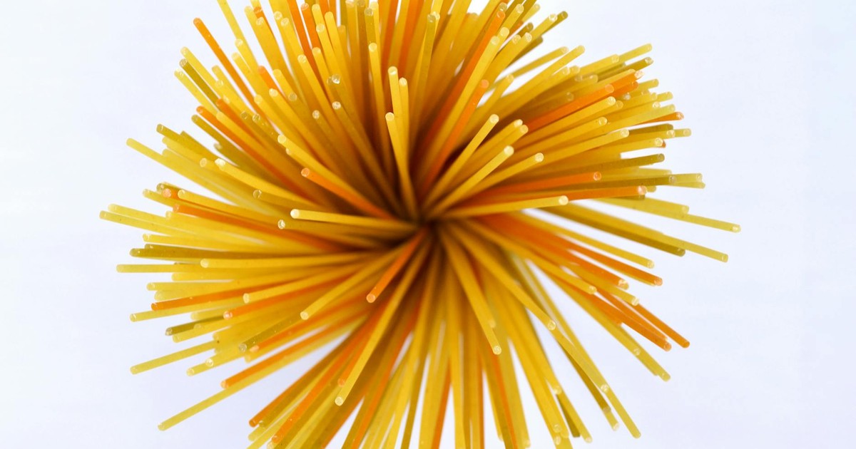 Close-up of vibrant yellow and orange uncooked spaghetti against a white background.
