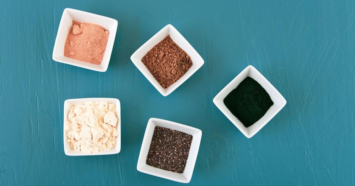 Aerial view of various spices presented in white bowls on a teal background, showcasing culinary diversity.