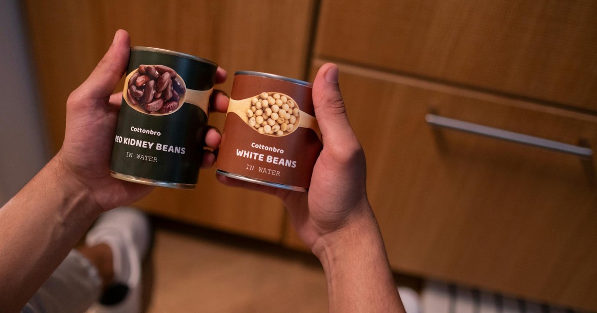 A person holding canned red kidney beans and white beans in a kitchen setting, emphasizing food storage.
