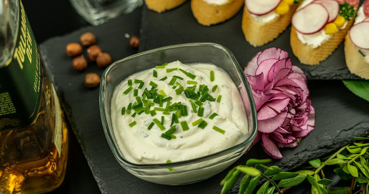 Close-up of creamy dip in glass bowl with herbs, elegant appetizers and decorative flower.
