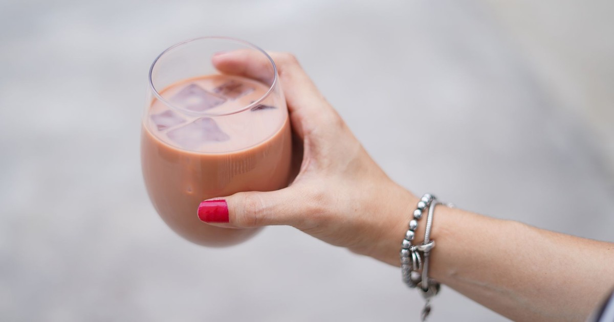 Close-up of a woman's hand holding a glass of iced coffee with bracelets, outdoors.