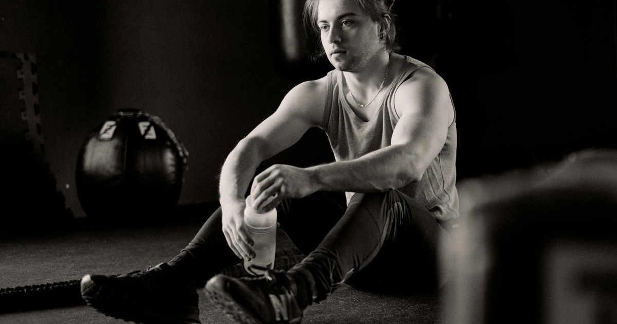 A young man sitting in a gym, resting after an intense workout session, holding a water bottle.